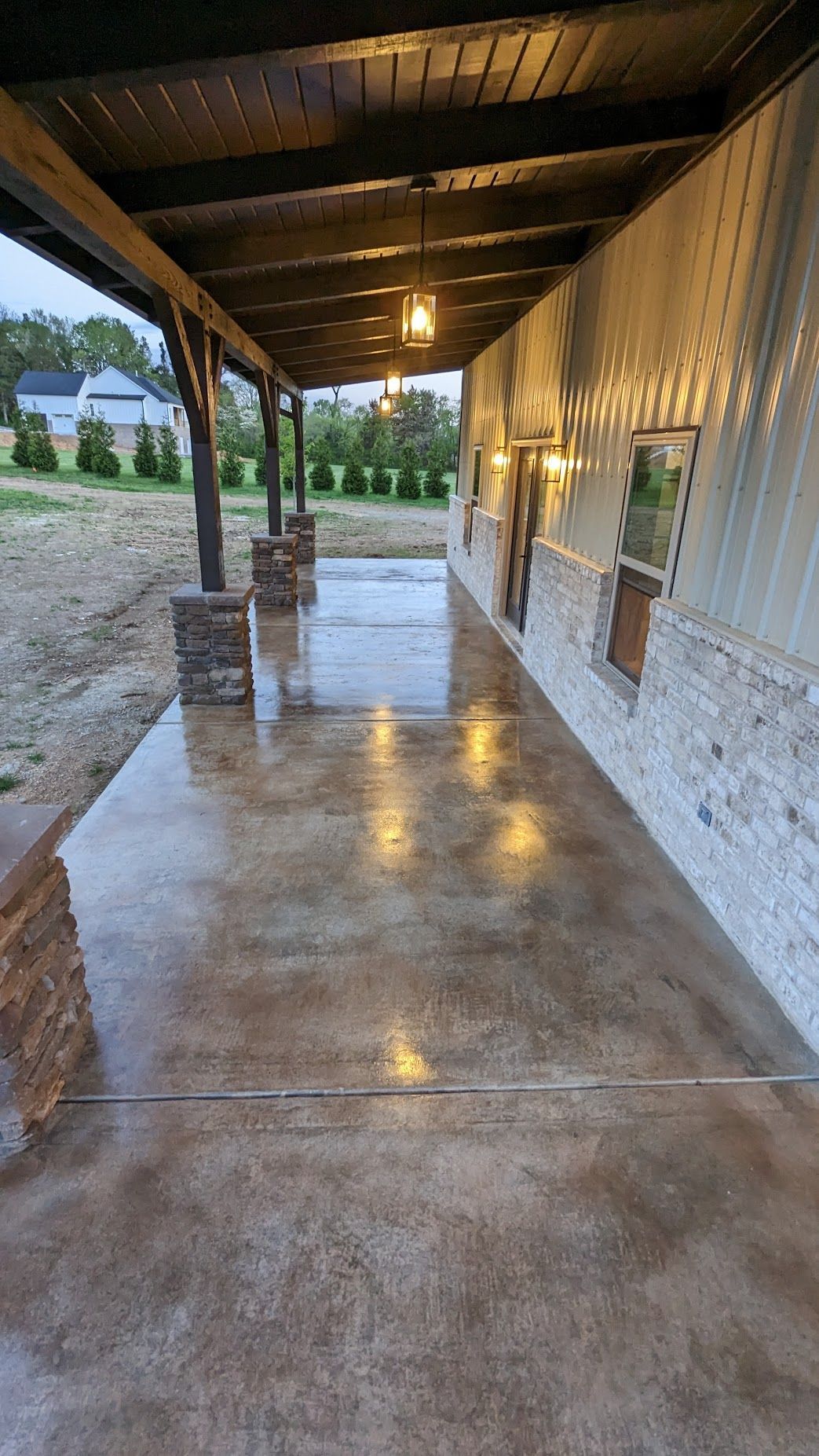 Covered patio with wet, textured concrete floor; stonework columns and accents. Building has glass block and warm lighting.
