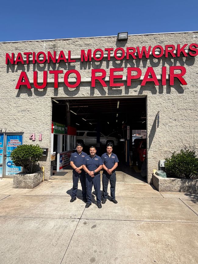 The beige exterior of National Motorworks Auto Repair with red lettering on a sunny day.
