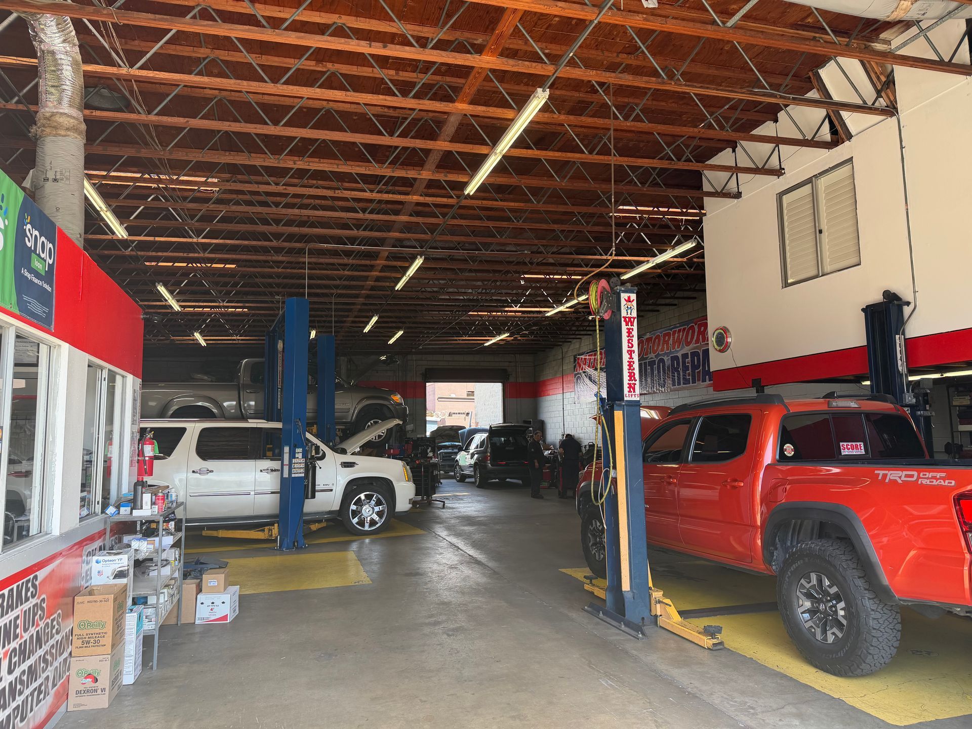 A brightly lit car repair shop with a white SUV and a bright orange pickup truck parked in service bays.