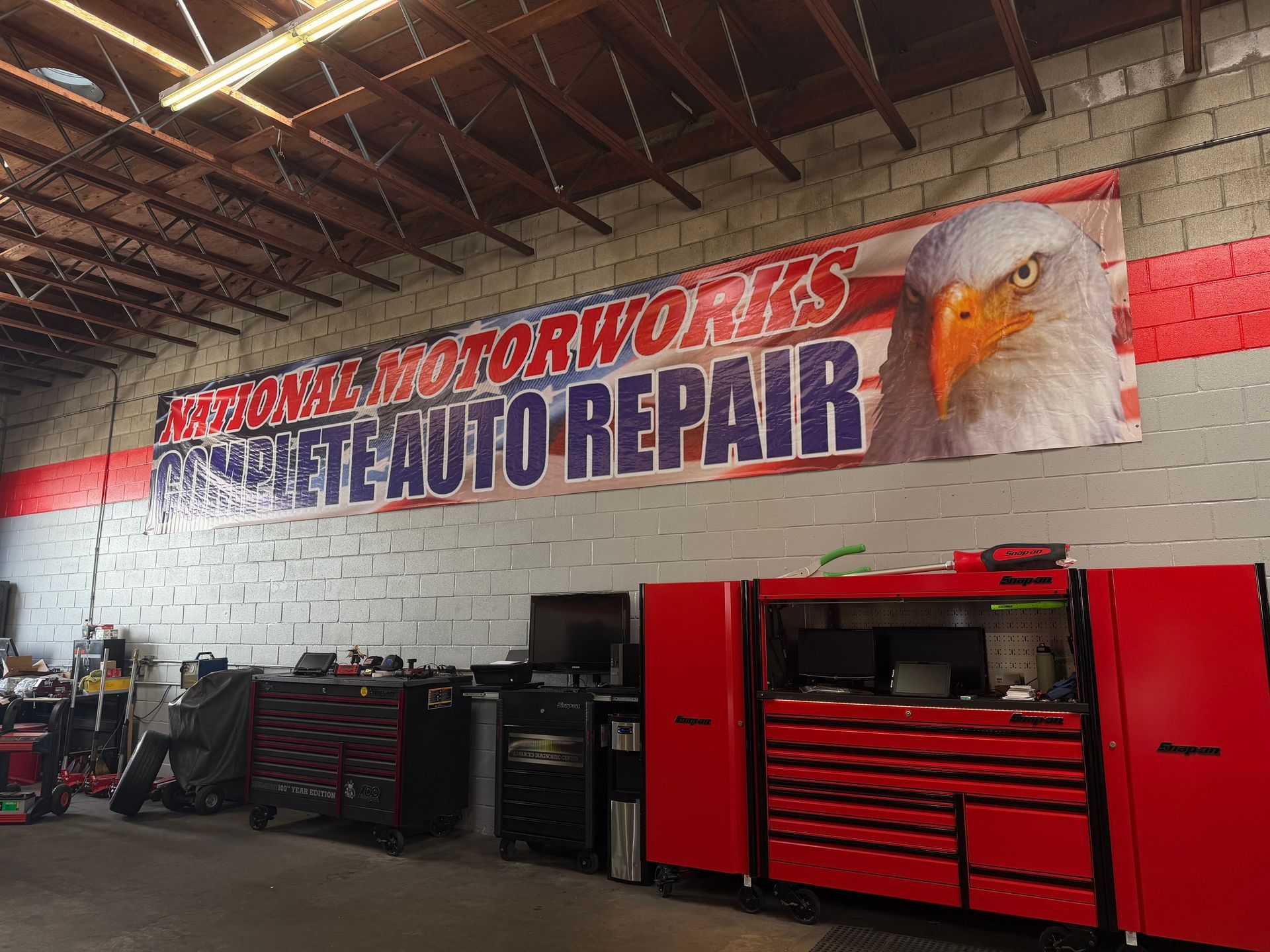 A white SUV lifted on a mechanical rack inside an auto repair shop with tools and a sign on the back wall.