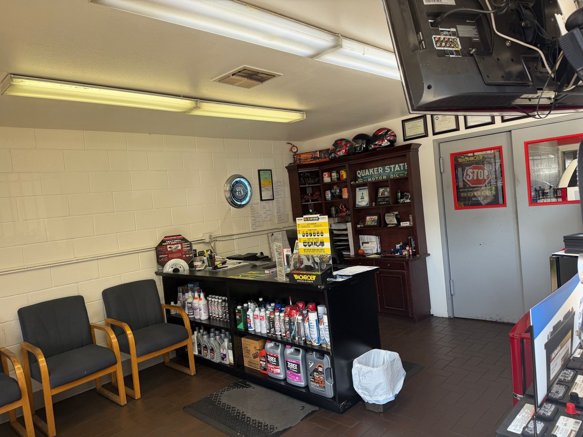 A waiting area with two gray chairs, a sales counter displaying automotive supplies, and shelving units in the background.