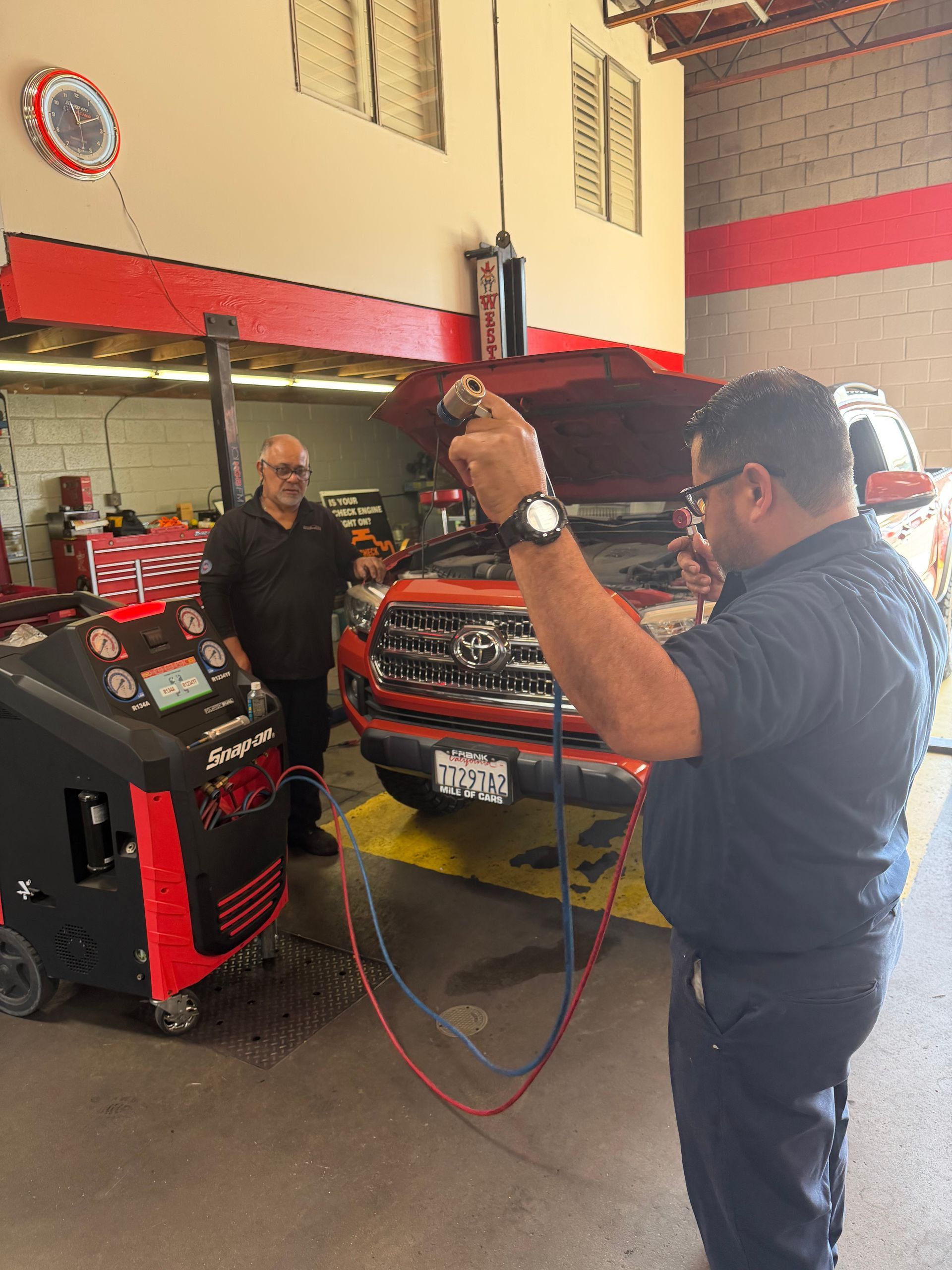 A mechanic in a blue shirt uses a digital diagnostic tablet to inspect the engine of an orange pickup truck in a garage.
