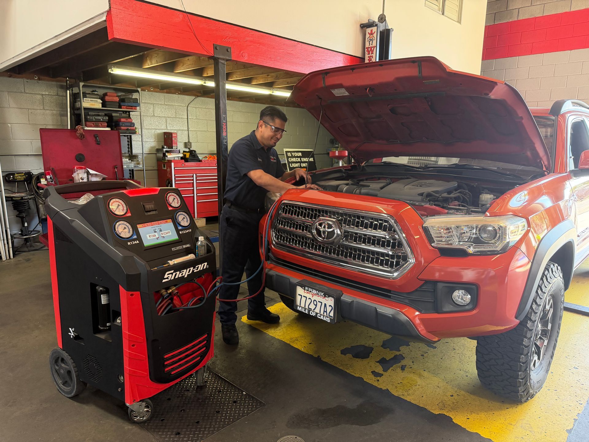 A technician in a blue uniform uses a pneumatic impact wrench to remove lug nuts from a lifted white truck’s wheel.
