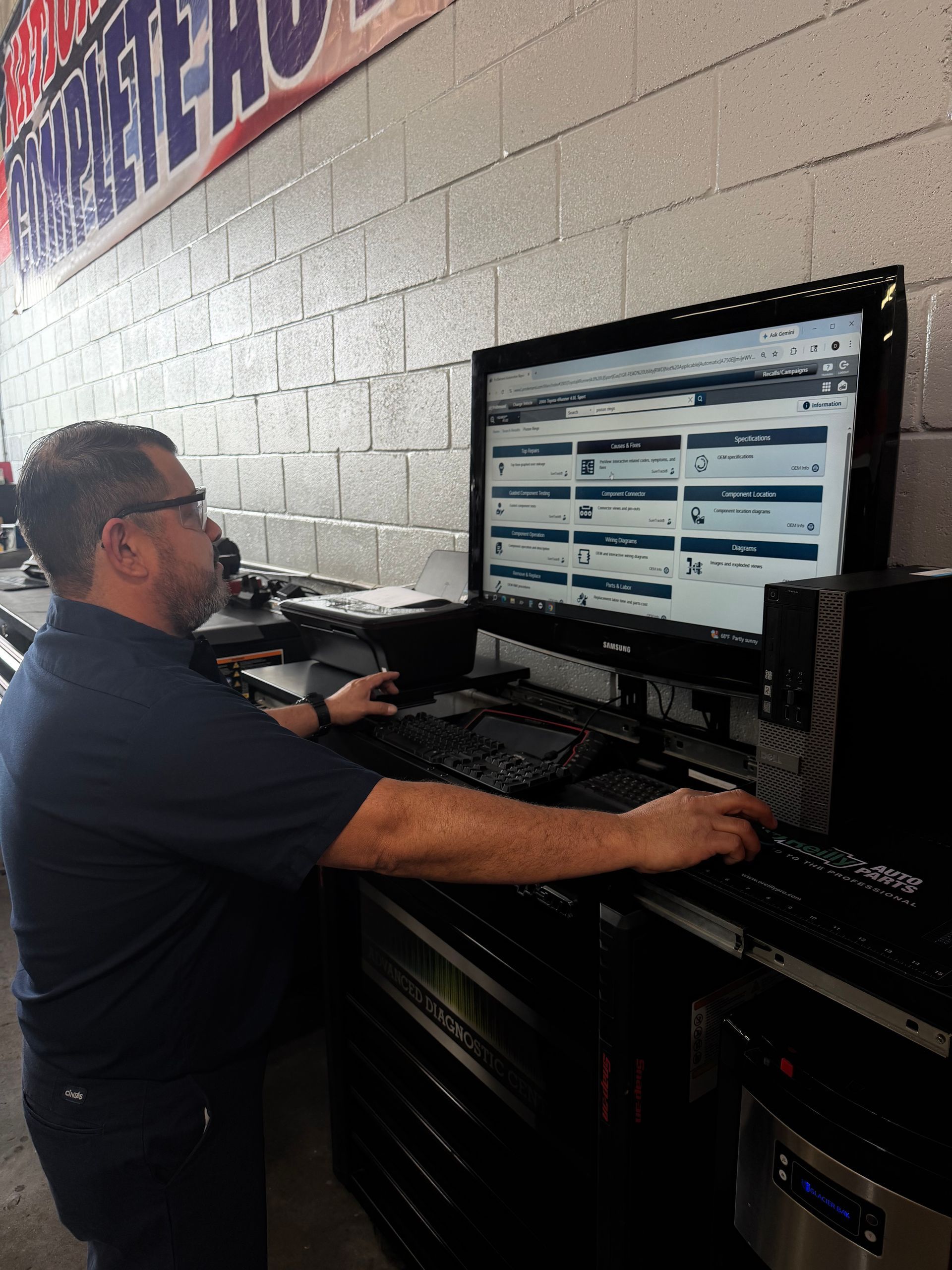 Two technicians working on a red vehicle's air conditioning system in an auto repair shop with an A/C service machine.