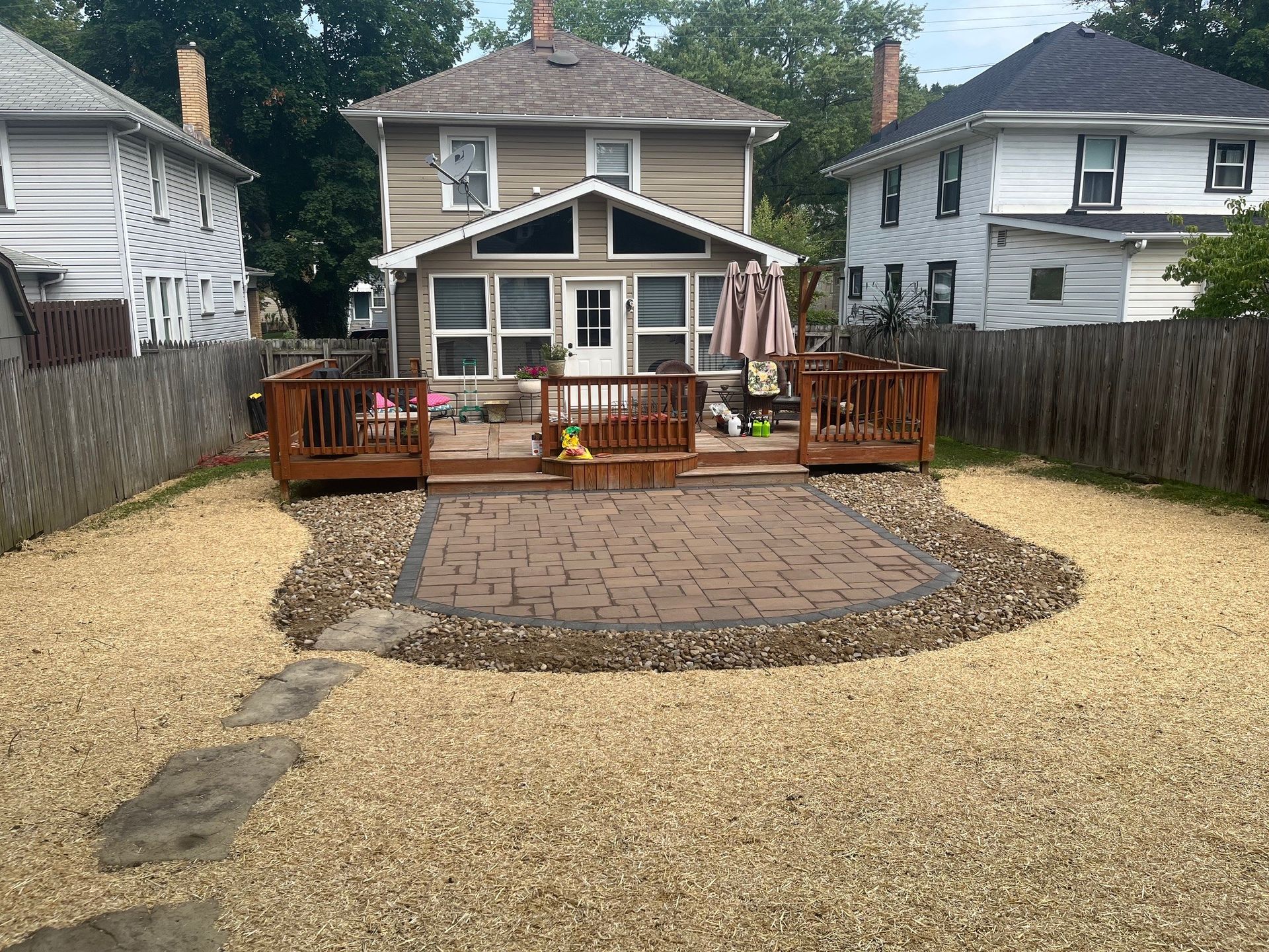 A tan house with a central patio and wooden deck, surrounded by a light-colored gravel yard and enclosed by fences.