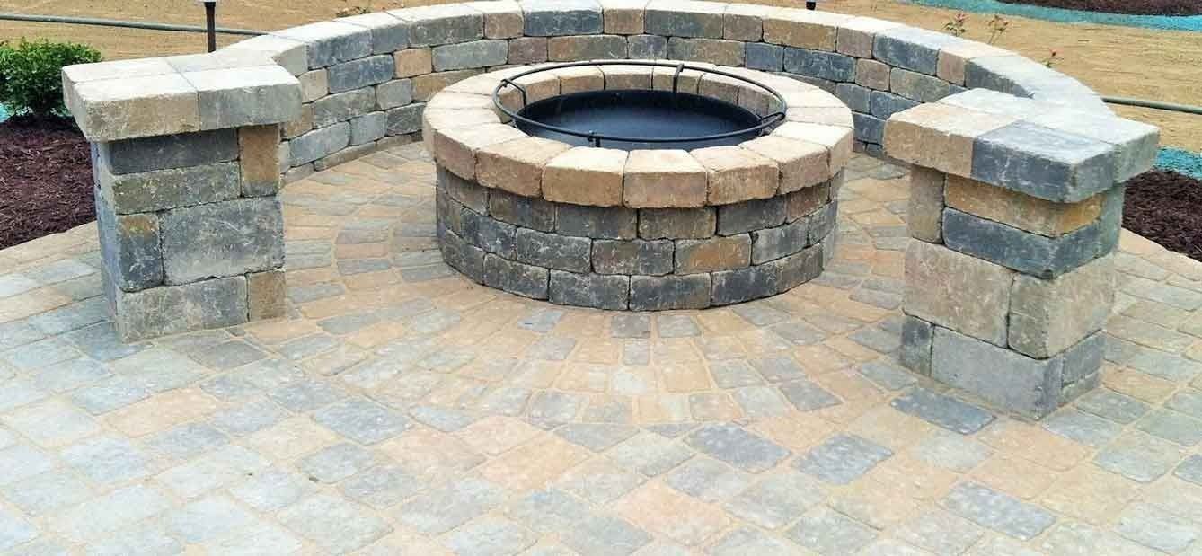 Fire pit with curved surrounding wall and pillars on a paved patio.