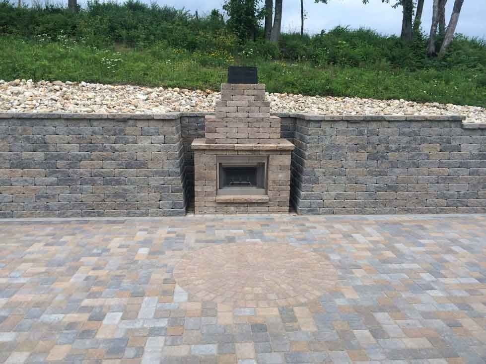 Stone patio with outdoor furniture, fire pit, and landscaping. White fence in the background.