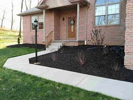 Brick house with a walkway, lamppost, and landscaping with dark mulch.