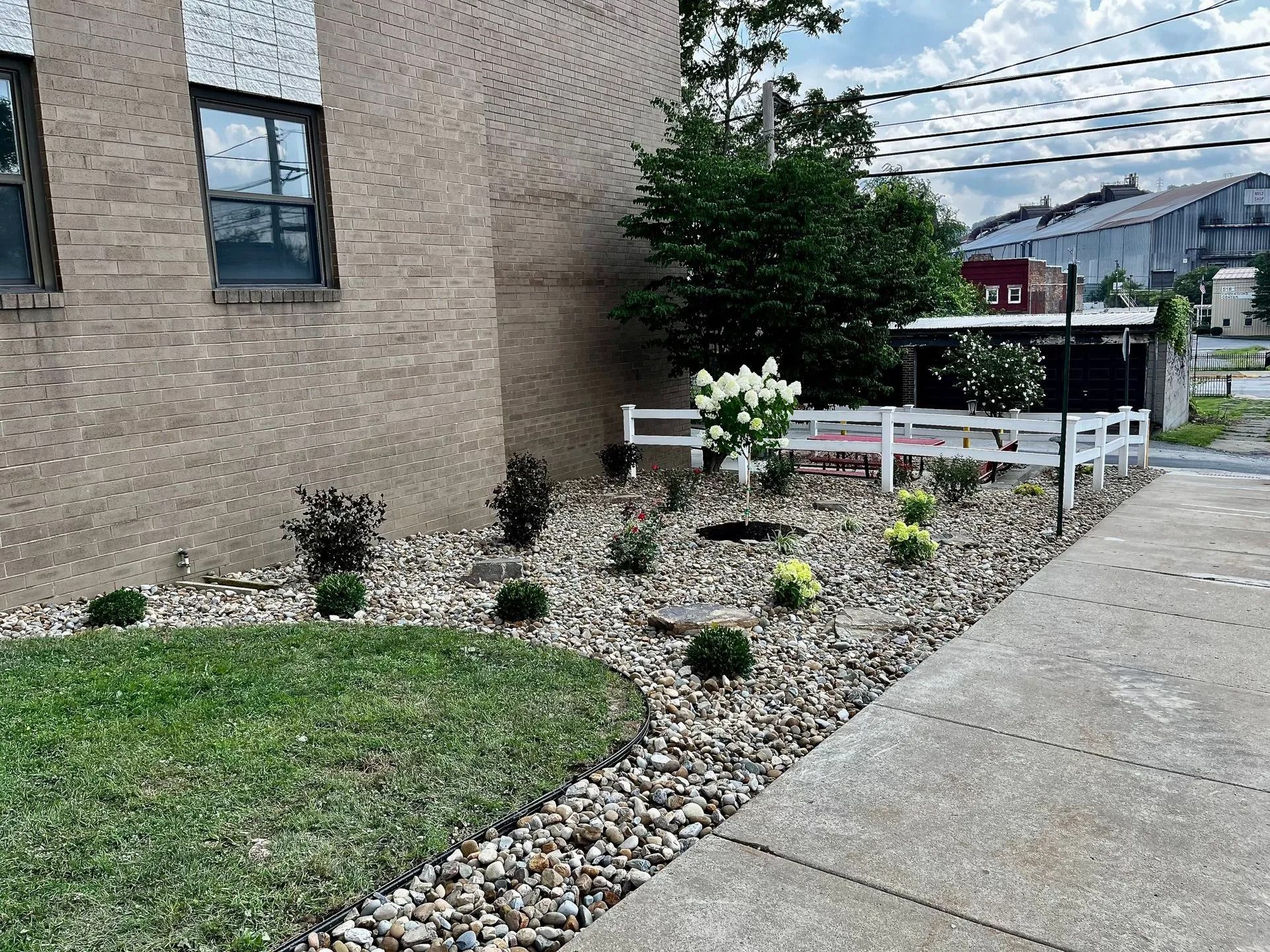 Brick building with landscaped flower bed of rocks and plants next to a sidewalk.