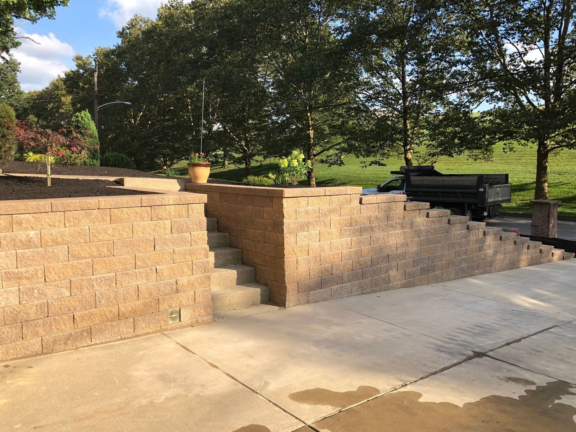 Concrete retaining walls with steps, concrete patio, trees and a truck in the background.