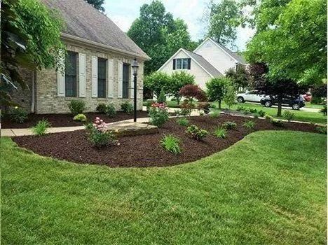 Landscaped yard with a brick house, mulch bed, and green grass.