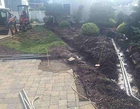 Construction site with a mini excavator, trenches, and mulch in a yard.