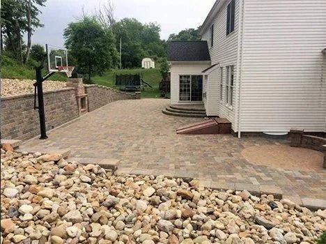 Stone patio with retaining wall, basketball hoop, and house.
