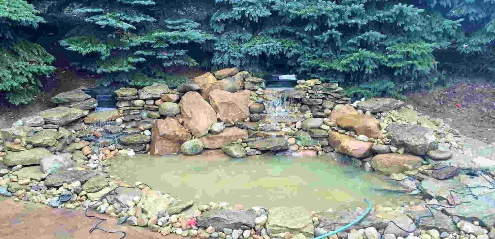 A pond with a waterfall, surrounded by rocks and trees.