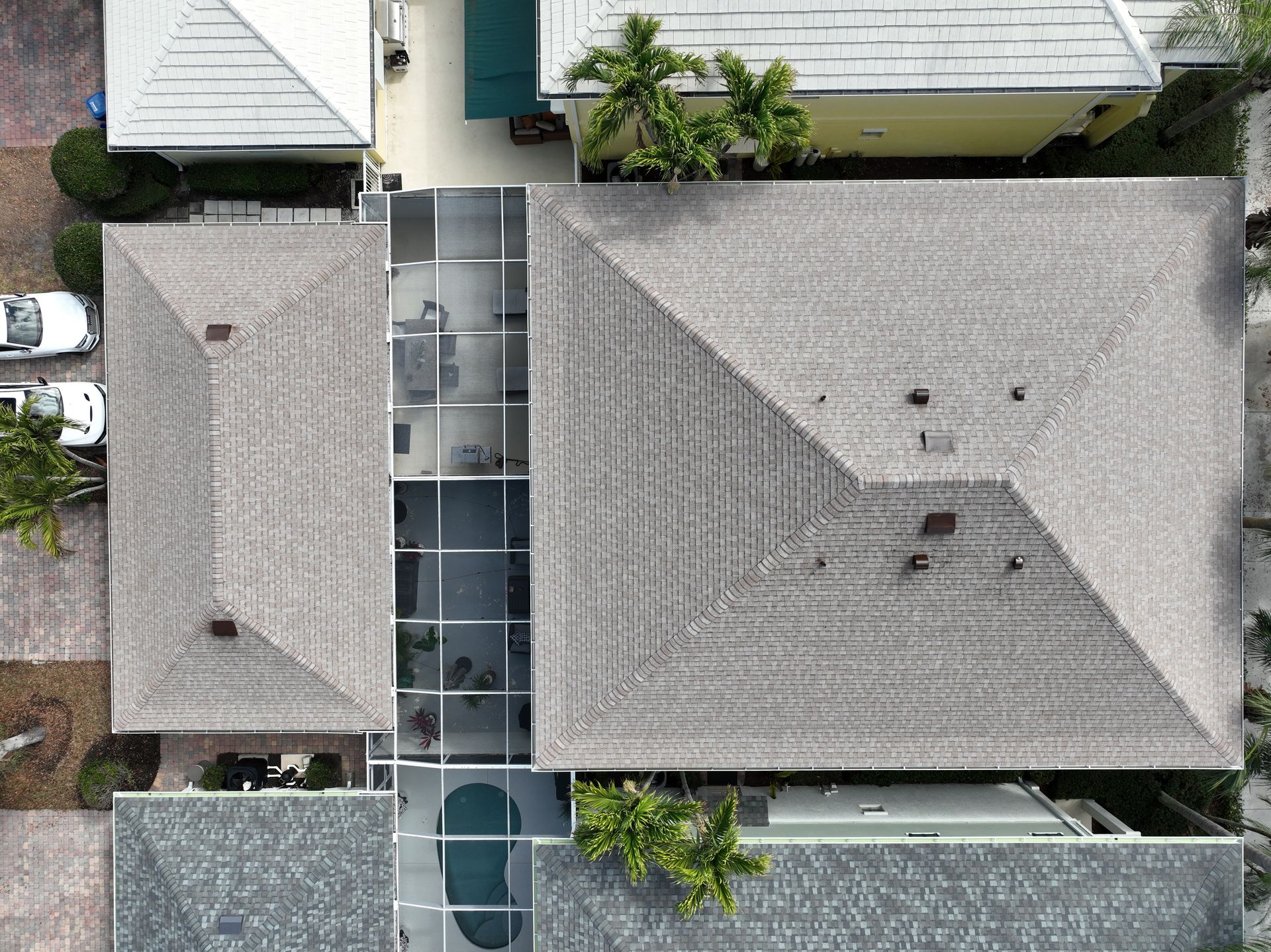 Aerial drone view of a gray asphalt shingle roof with screened lanai and pool in a Jupiter, FL