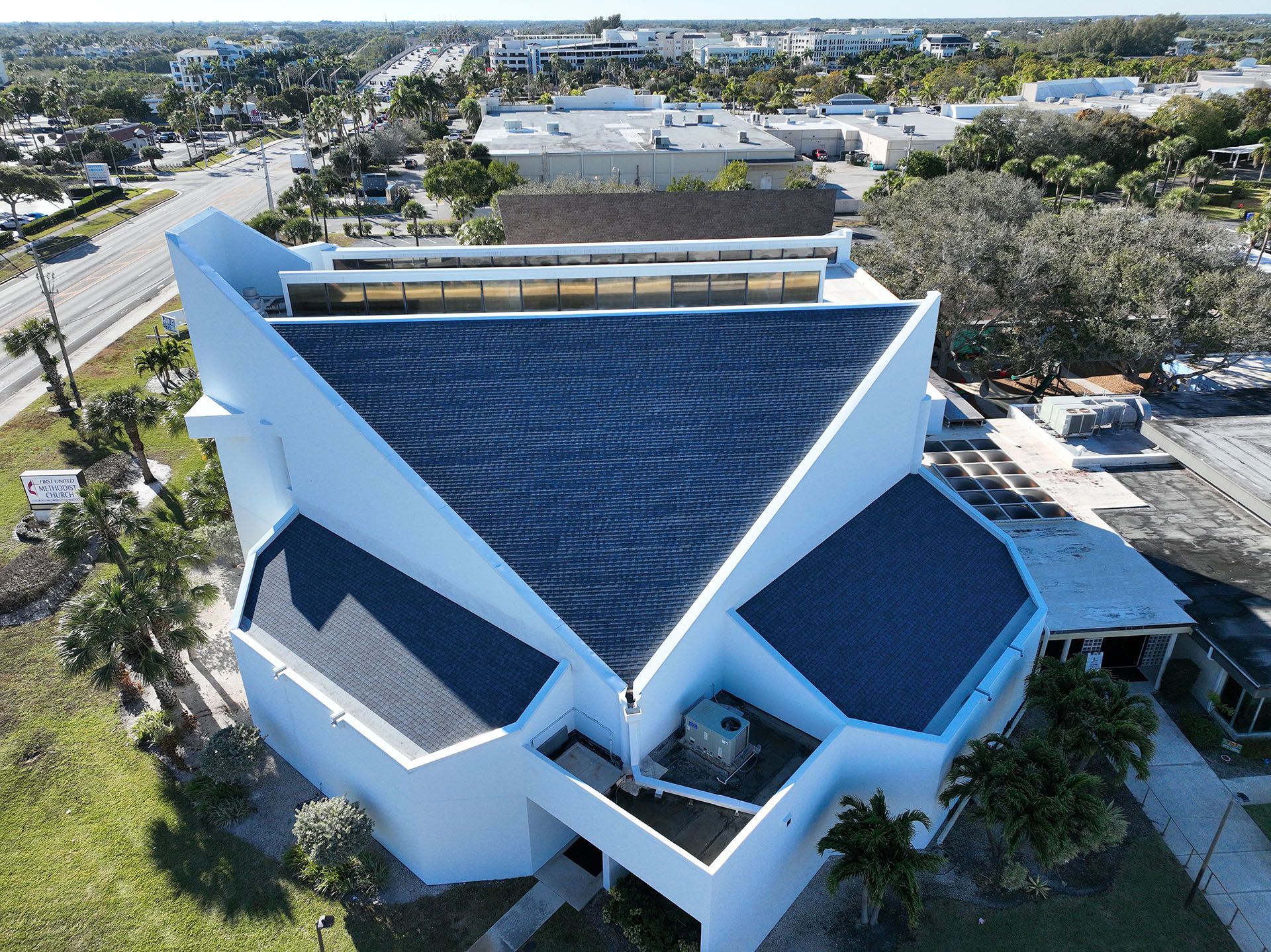 Aerial view of a white building with a unique geometric roof; sunny day.
