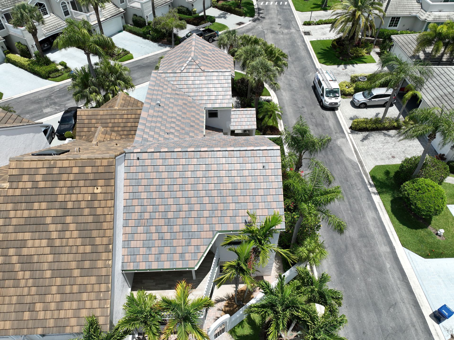 Aerial view of a house with a gray and brown shingle roof surrounded by palm trees and a street.