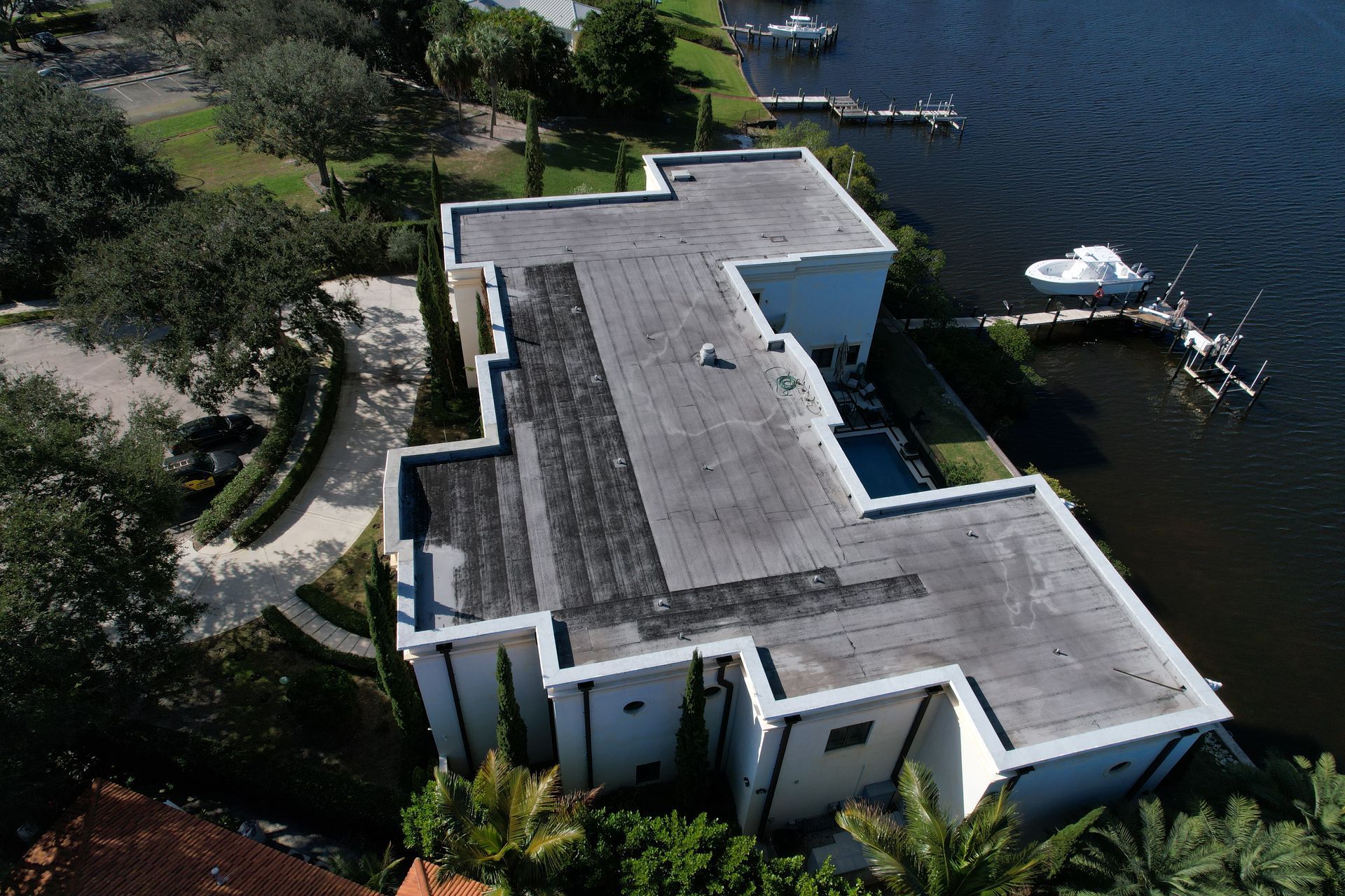 Aerial view of modern home with a flat roof on waterfront, boat docks visible.
