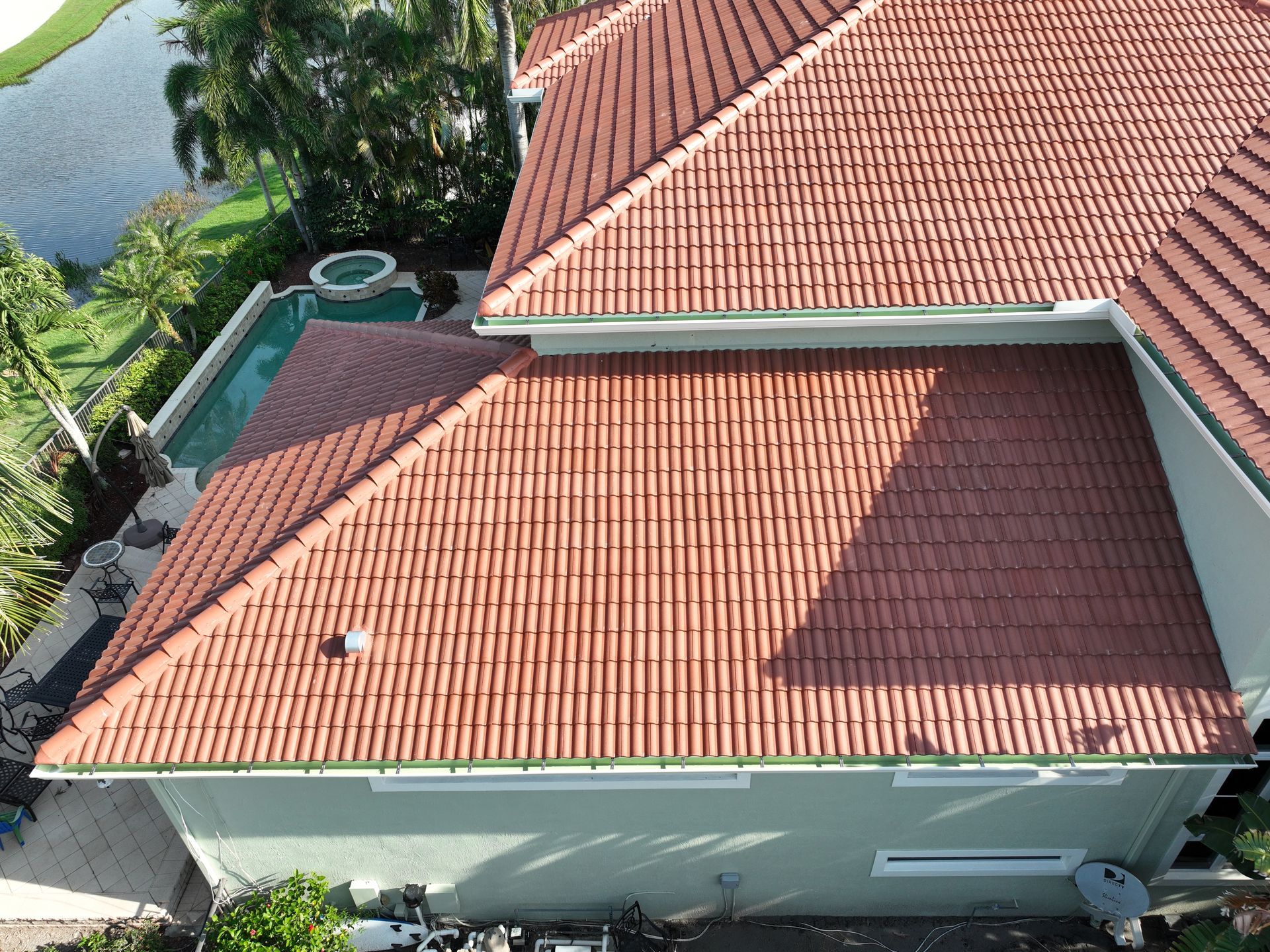 Red tile roof on a light green house, with a pool and lake visible in the background.