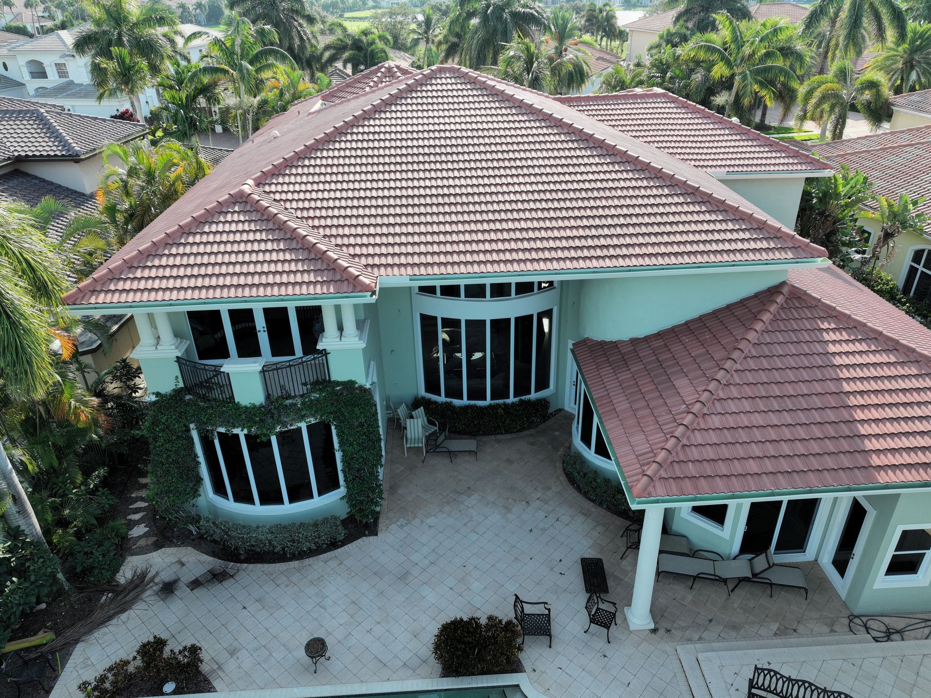 Large light green house with red tile roof, large windows, patio, and lush landscaping.