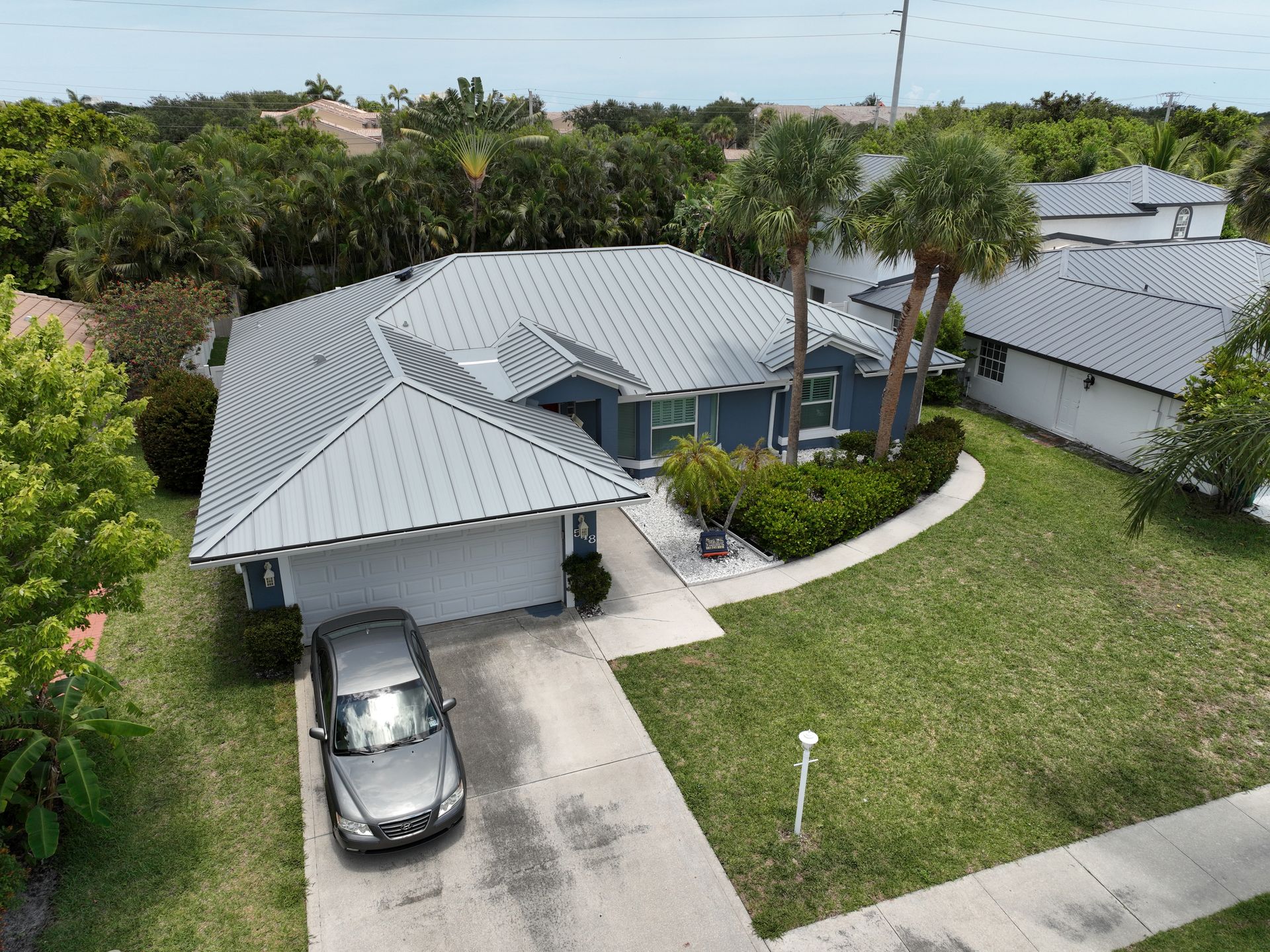 Aerial view of a grey house with a metal roof, a car in the driveway, and a well-kept lawn.