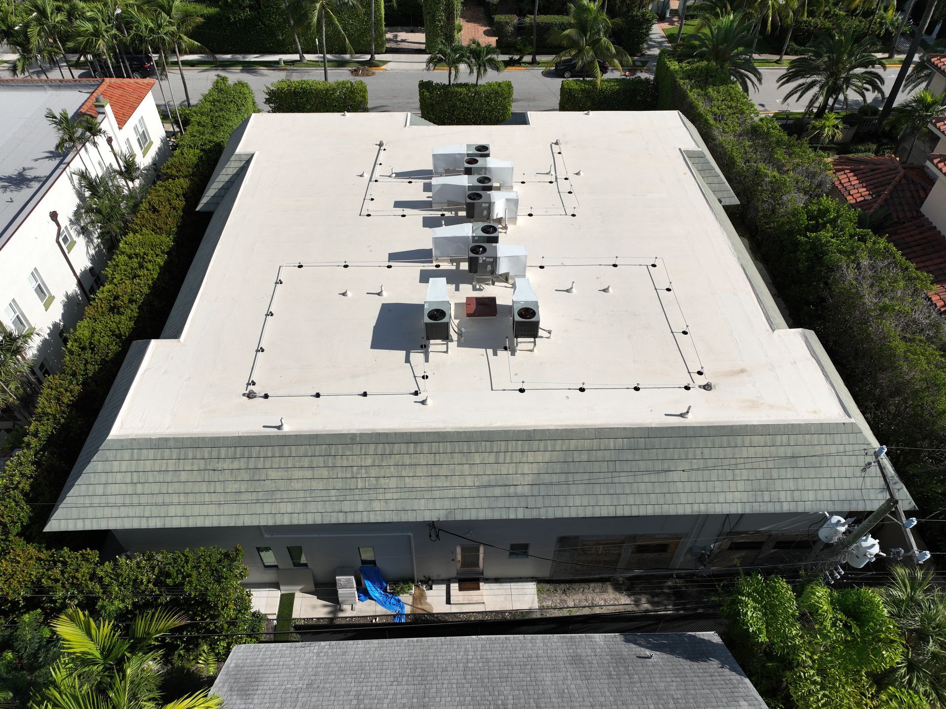 Aerial view of a flat roof with HVAC units. The house is surrounded by green hedges and trees.