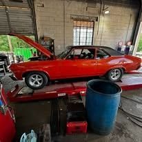 A red car is sitting on a lift in a garage.
