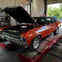 A red car with the hood up is sitting on a lift in a garage.