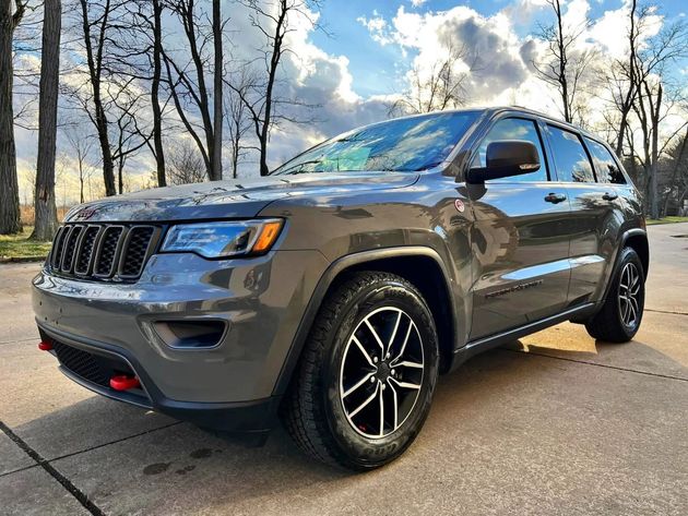 Gray Jeep Grand Cherokee SUV parked outdoors with black wheels and a red tow hook.