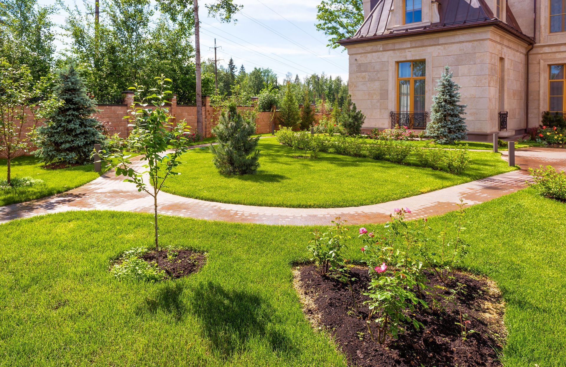 Well-manicured lawn with curved pathway, trees, and a stone house in the background.