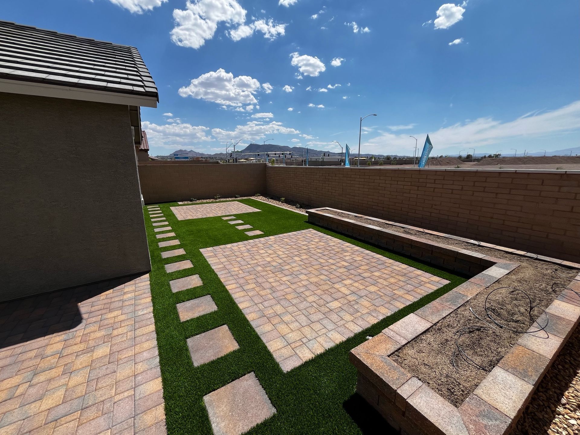 A backyard with a brick walkway and a bench.