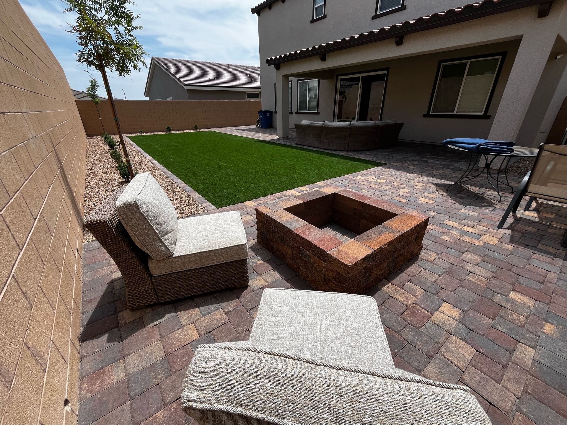 A patio with a fire pit and chairs in front of a house.