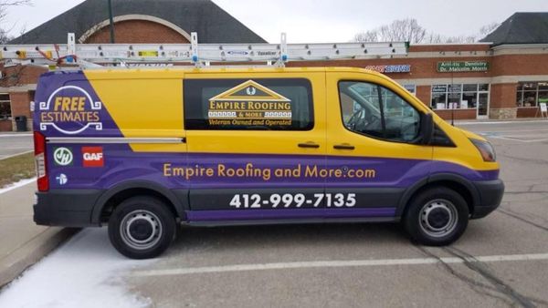 Yellow and purple Empire Roofing van with ladder parked in front of a shopping center.
