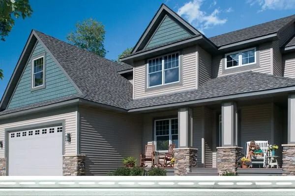 Two-story house with blue-green gables, gray siding, stone pillars, and a white garage door.