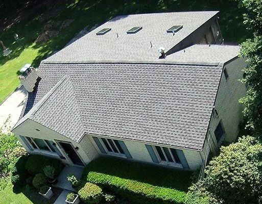 An aerial view of a house with a gray shingled roof, skylights, and landscaping.