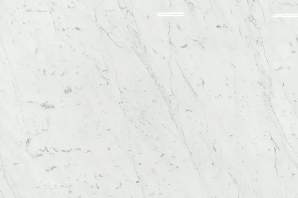 White marble surface with subtle gray veining and a small light reflection near the top center
