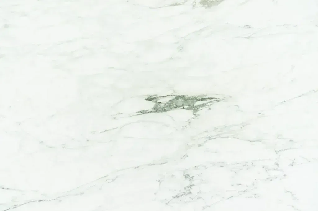 White marble surface with subtle gray veining and a small greenish stain near the center