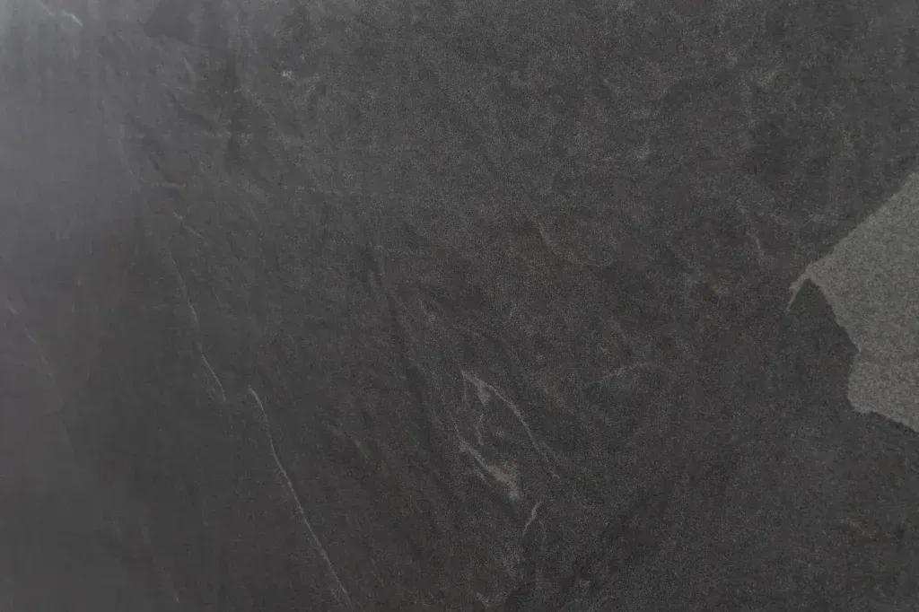 Dark gray textured surface with faint scratches and a small lighter patch at the right edge