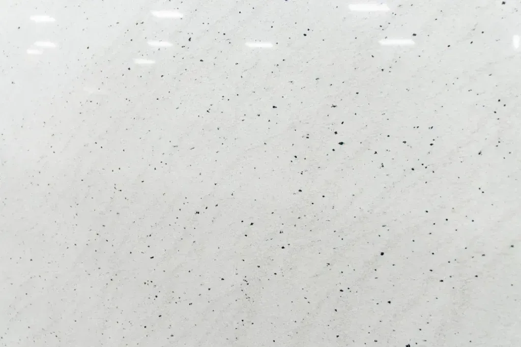 Light gray speckled surface with scattered small dark flecks and soft reflections