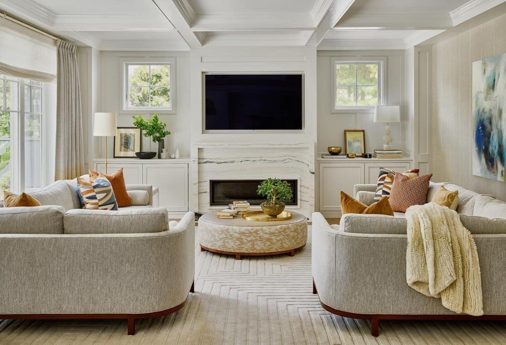 Bright living room with white sofas, fireplace, wall-mounted TV, and large windows