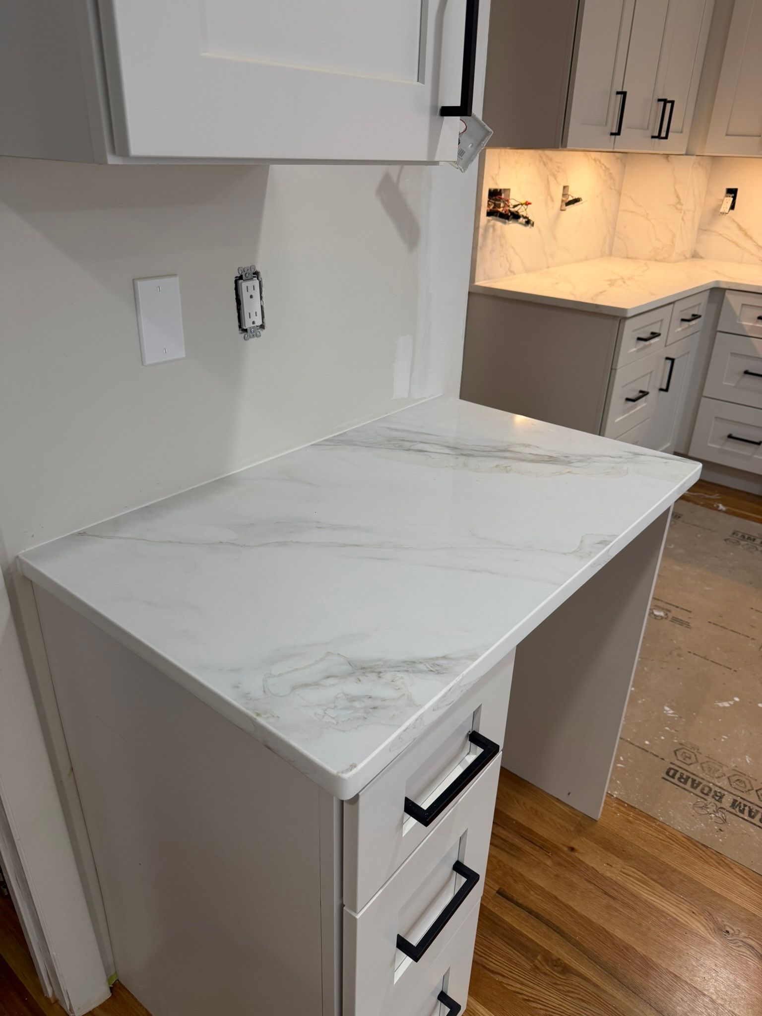 White marble-top cabinet with drawers in a bright kitchen hallway, beside white cabinets and wood floors