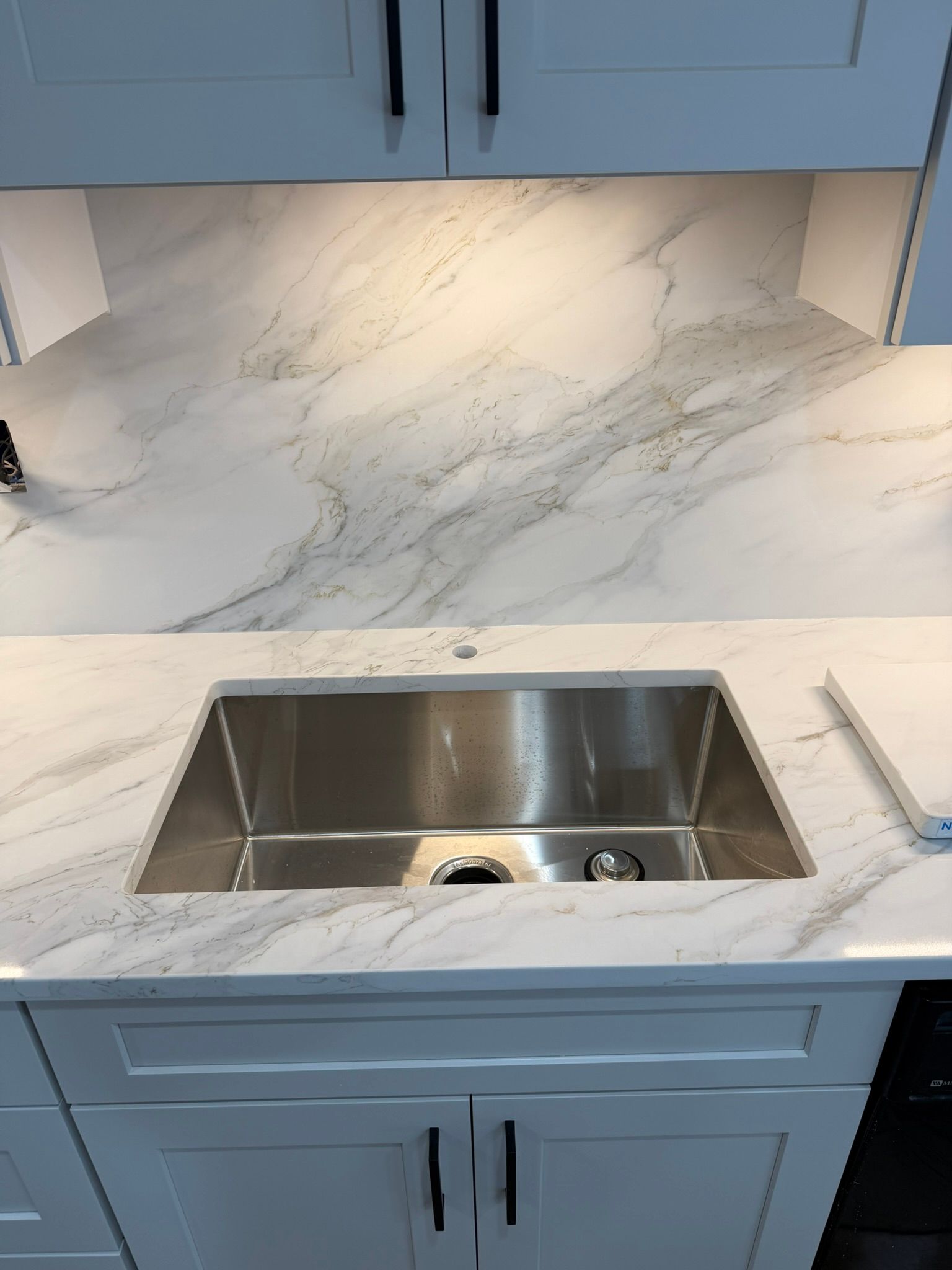 Kitchen countertop with white marble-look surface and stainless steel sink, surrounded by blue cabinets