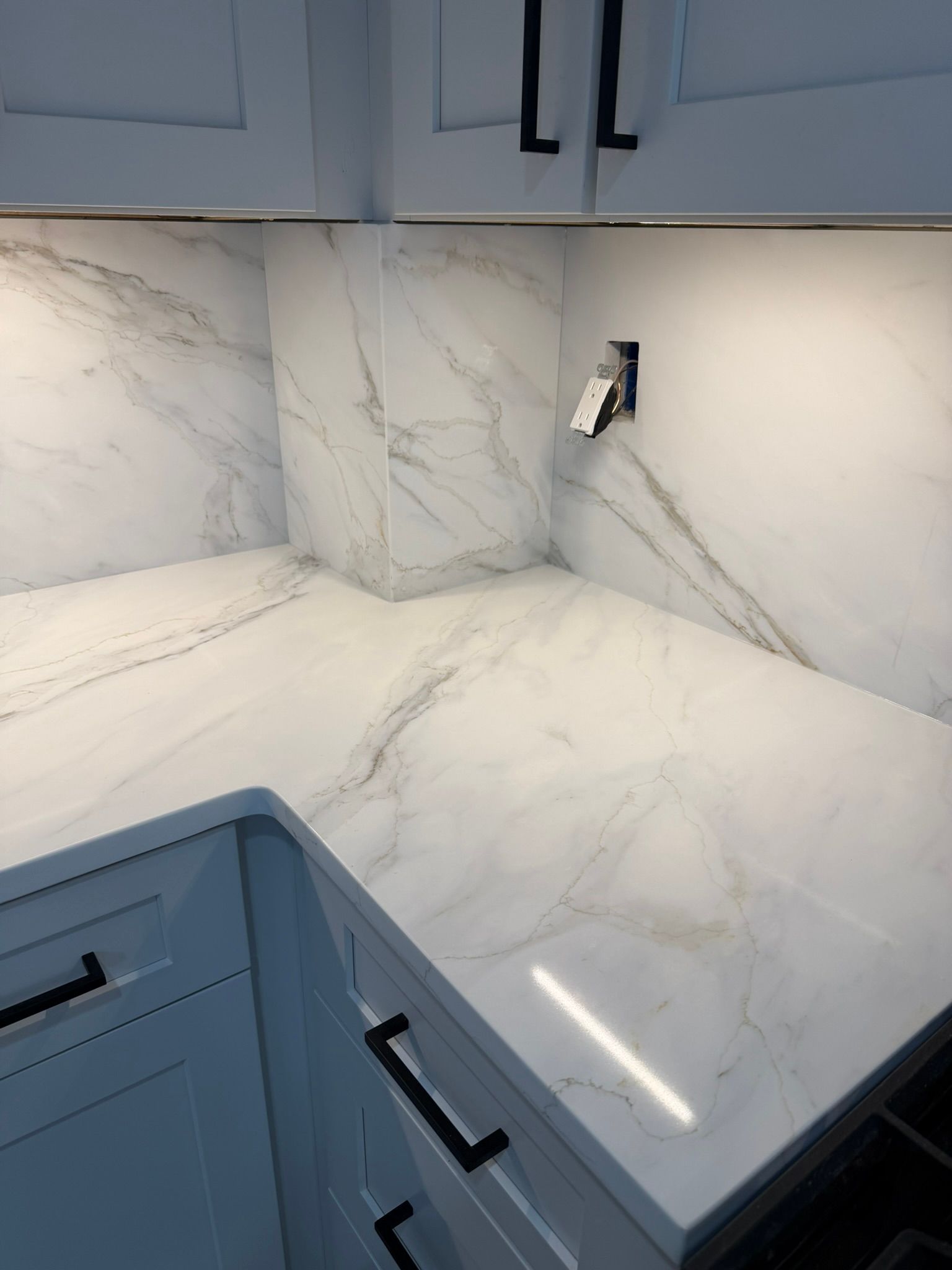 White marble-look kitchen corner with blue cabinets and black handles under under-cabinet lighting