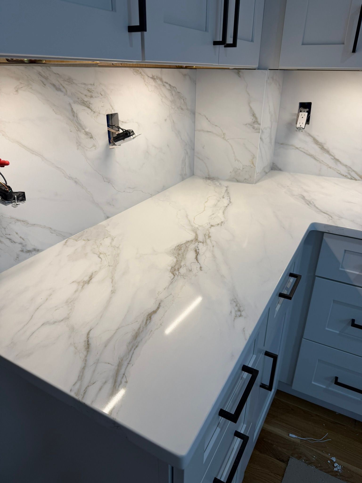 Modern kitchen with white marble-look countertops and backsplash, blue-gray cabinets, and wood flooring