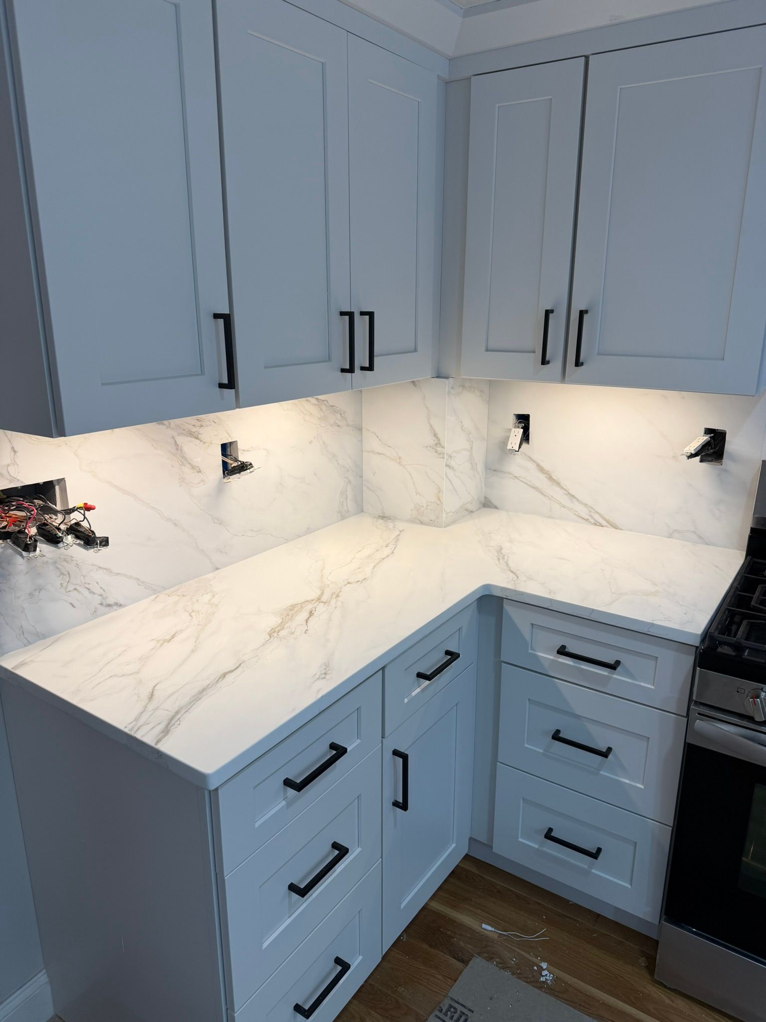 White kitchen corner with marble-look countertops, light blue cabinets, and under-cabinet lighting