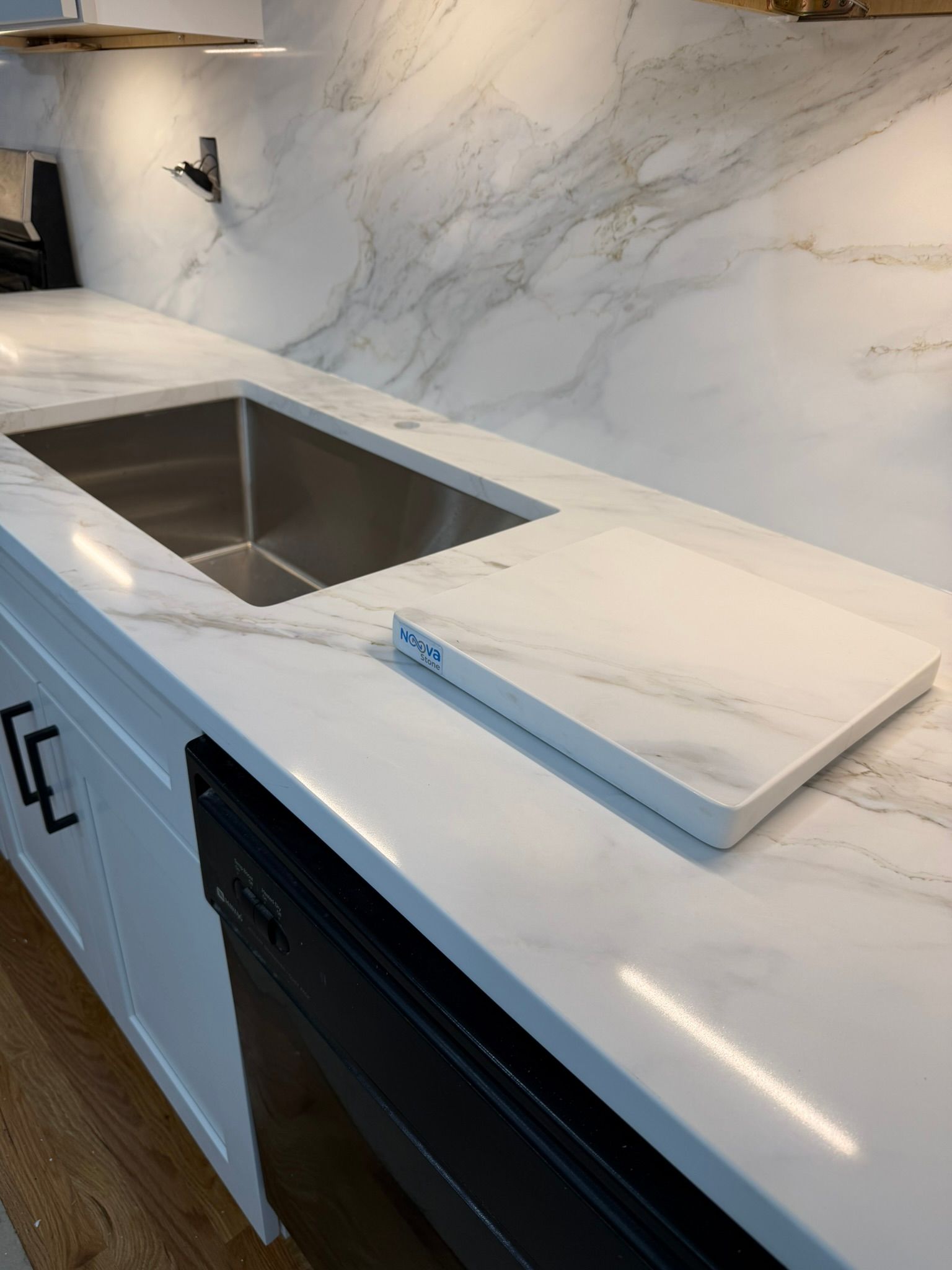 Modern kitchen countertop with stainless sink, marble backsplash, and black dishwasher under the counter