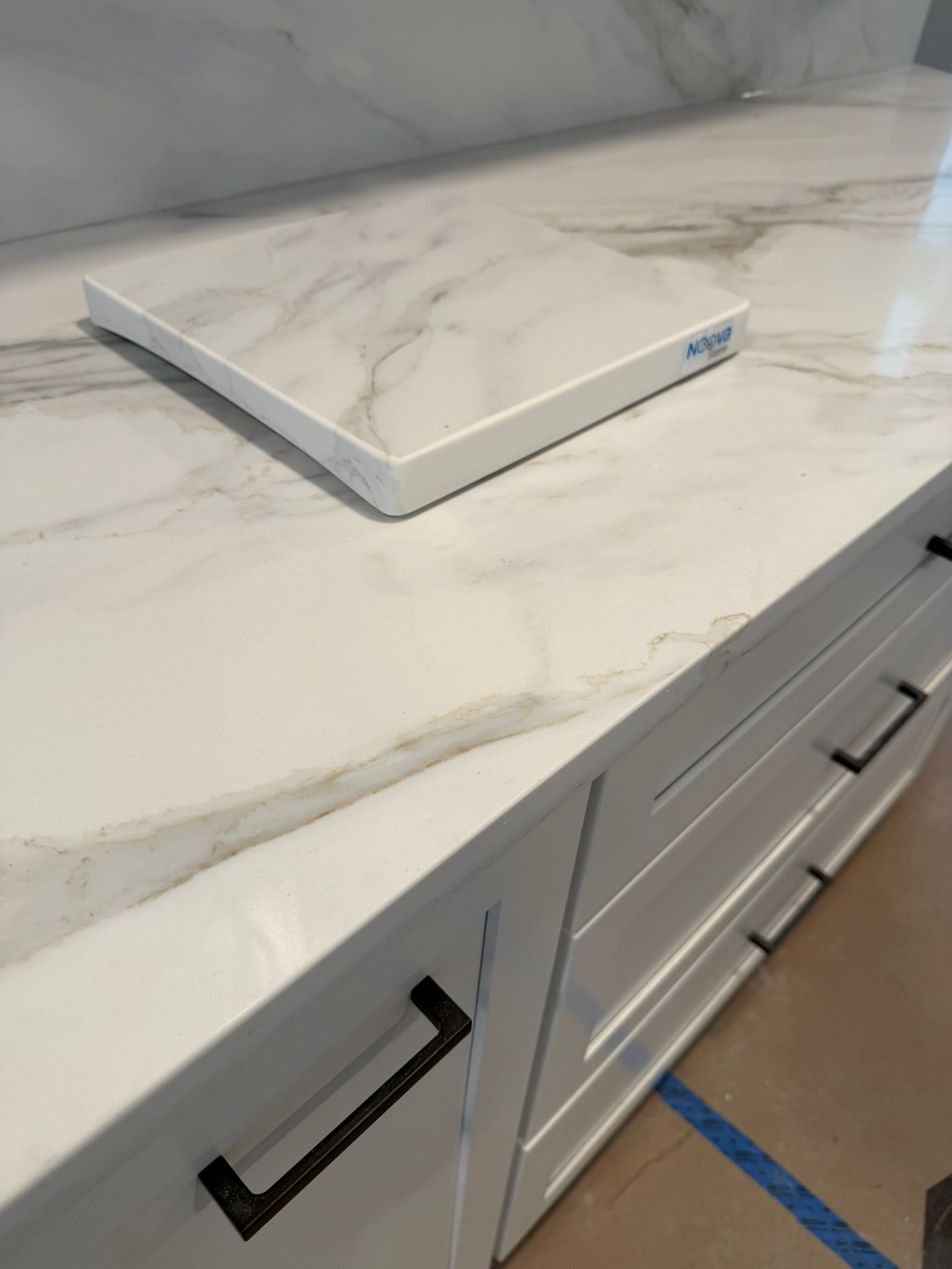 White marble cutting board on a light marble kitchen counter with white cabinets below