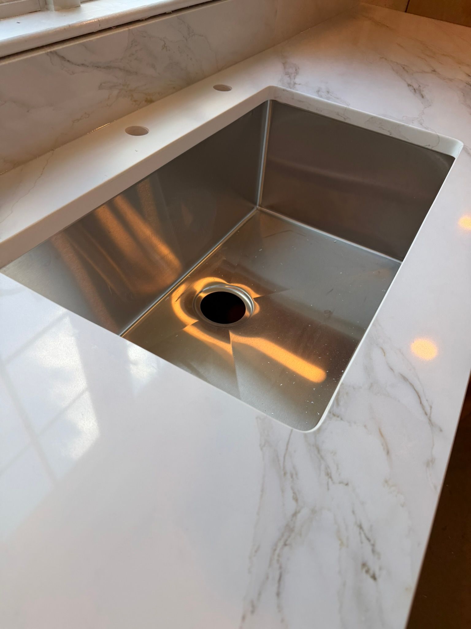 Stainless steel kitchen sink set in a white marble countertop with a faucet hole visible.