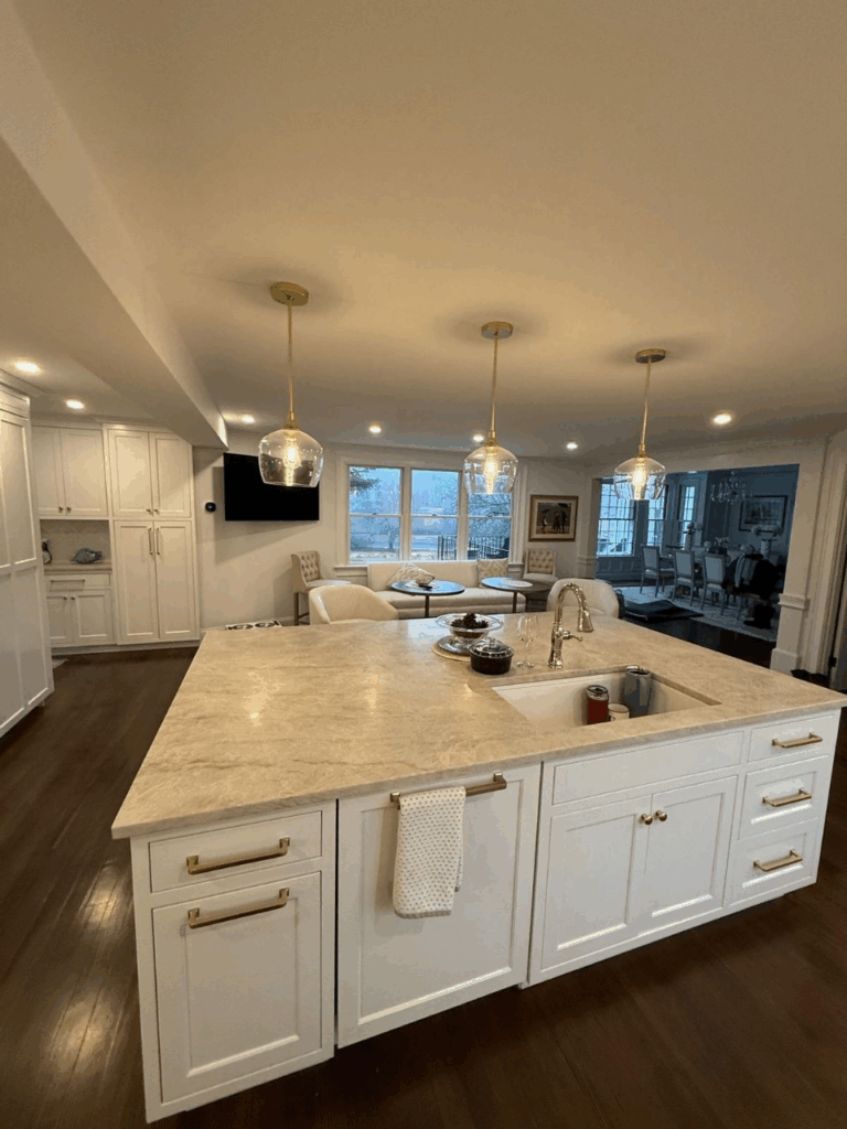 Bright modern kitchen with large island, white cabinets, pendant lights, and a dining area in the background