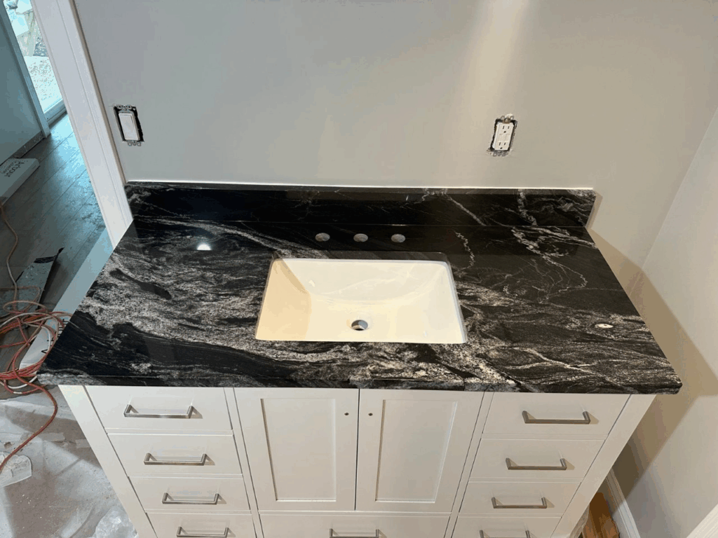 Bathroom vanity with black marble countertop, white sink, and white cabinet drawers being installed